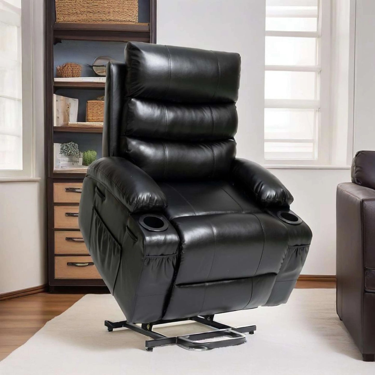 Black faux leather power lift recliner chair in full lift position in a living room setting with a bookshelf and window in the background.