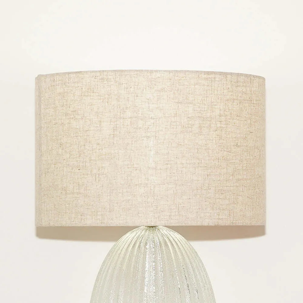 Table lamp with a beige fabric shade and ribbed glass base on a white background
