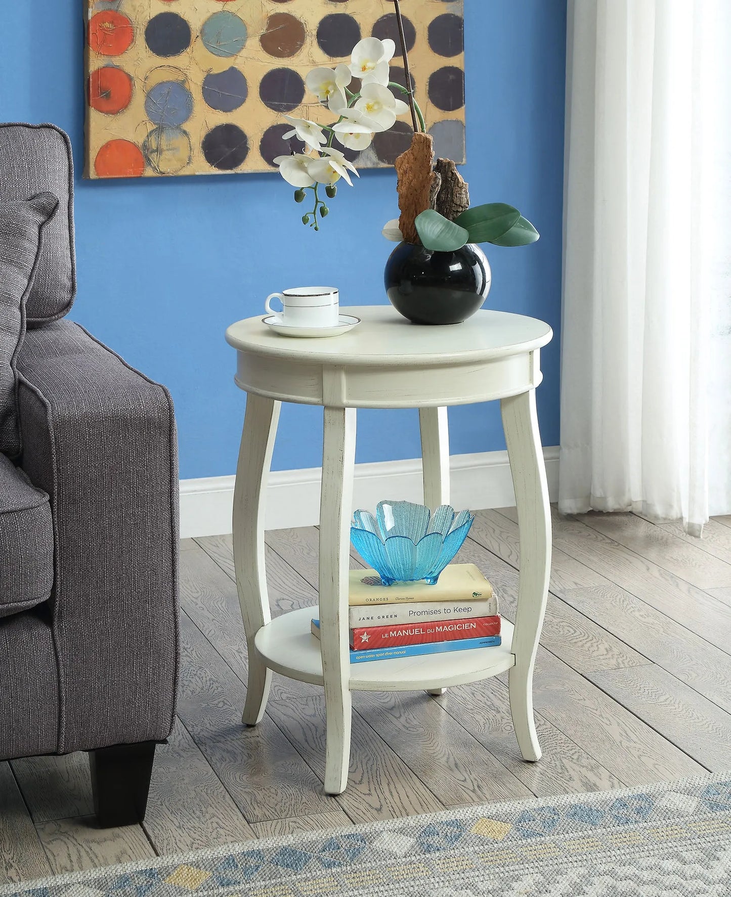 Antique white end table with decor items next to a gray sofa against a blue wall.