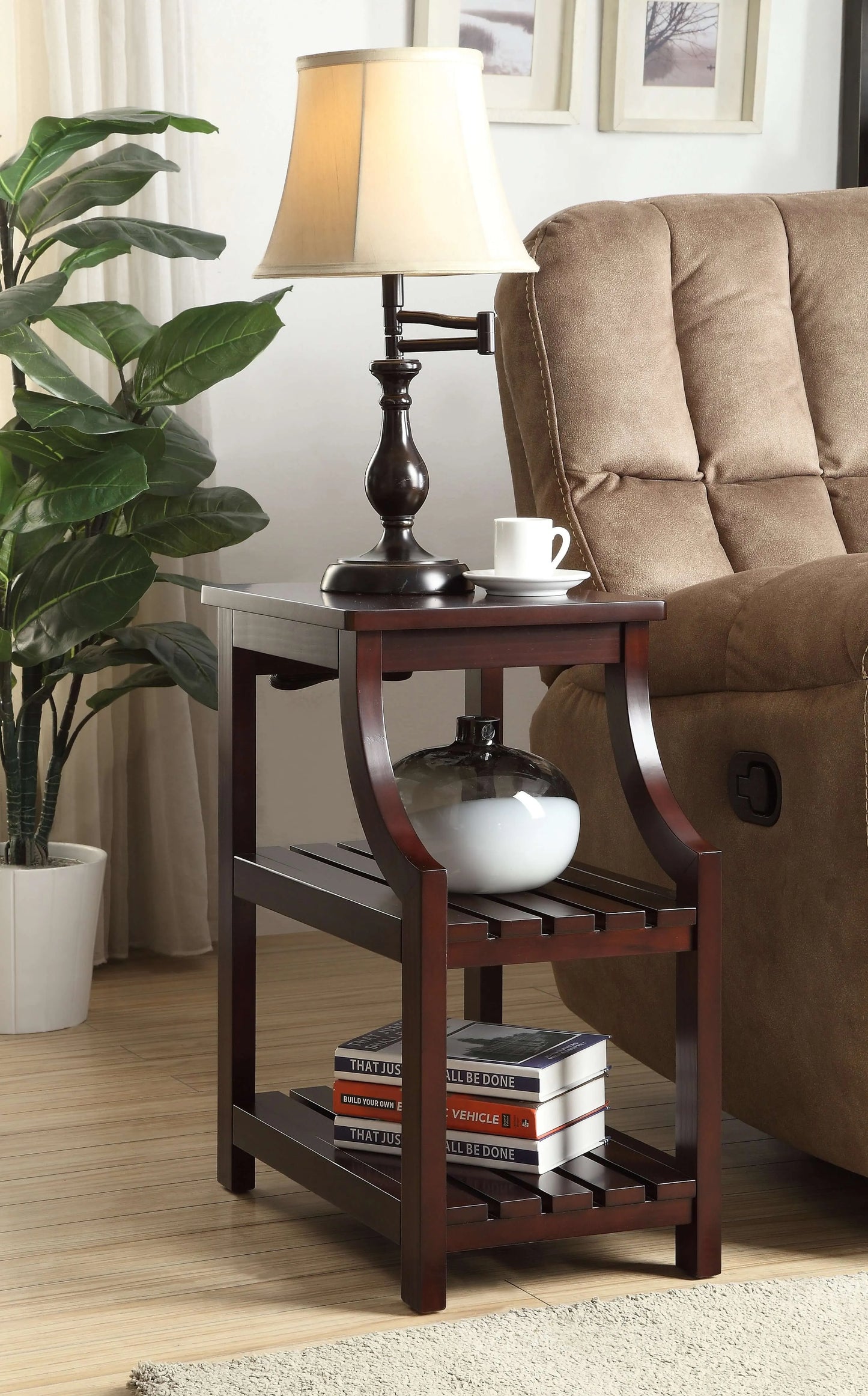 Wooden end table with lamp and books next to a brown sofa and plant