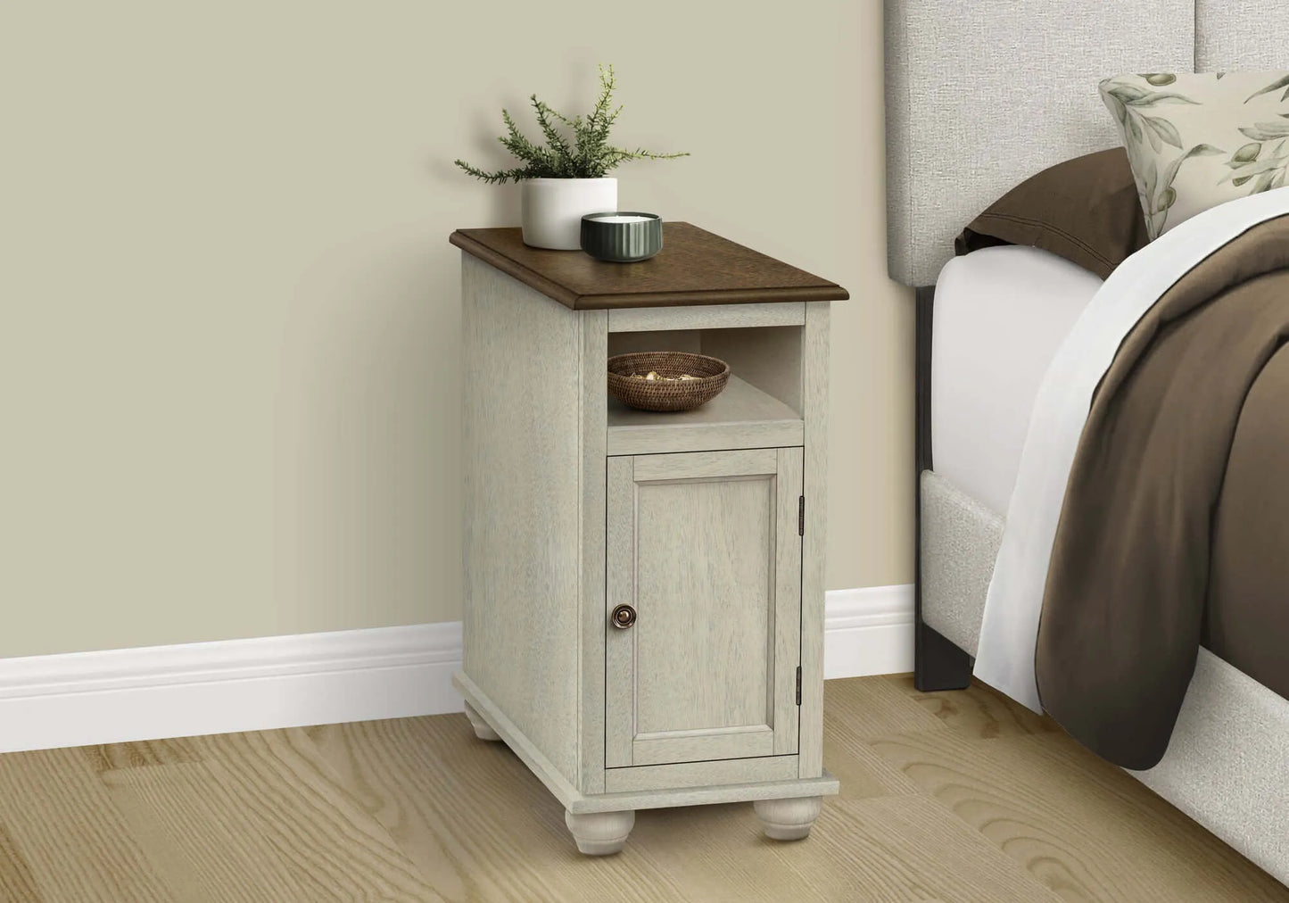 Small end table / nightstand with a cabinet door next to a bed with brown bedding.
