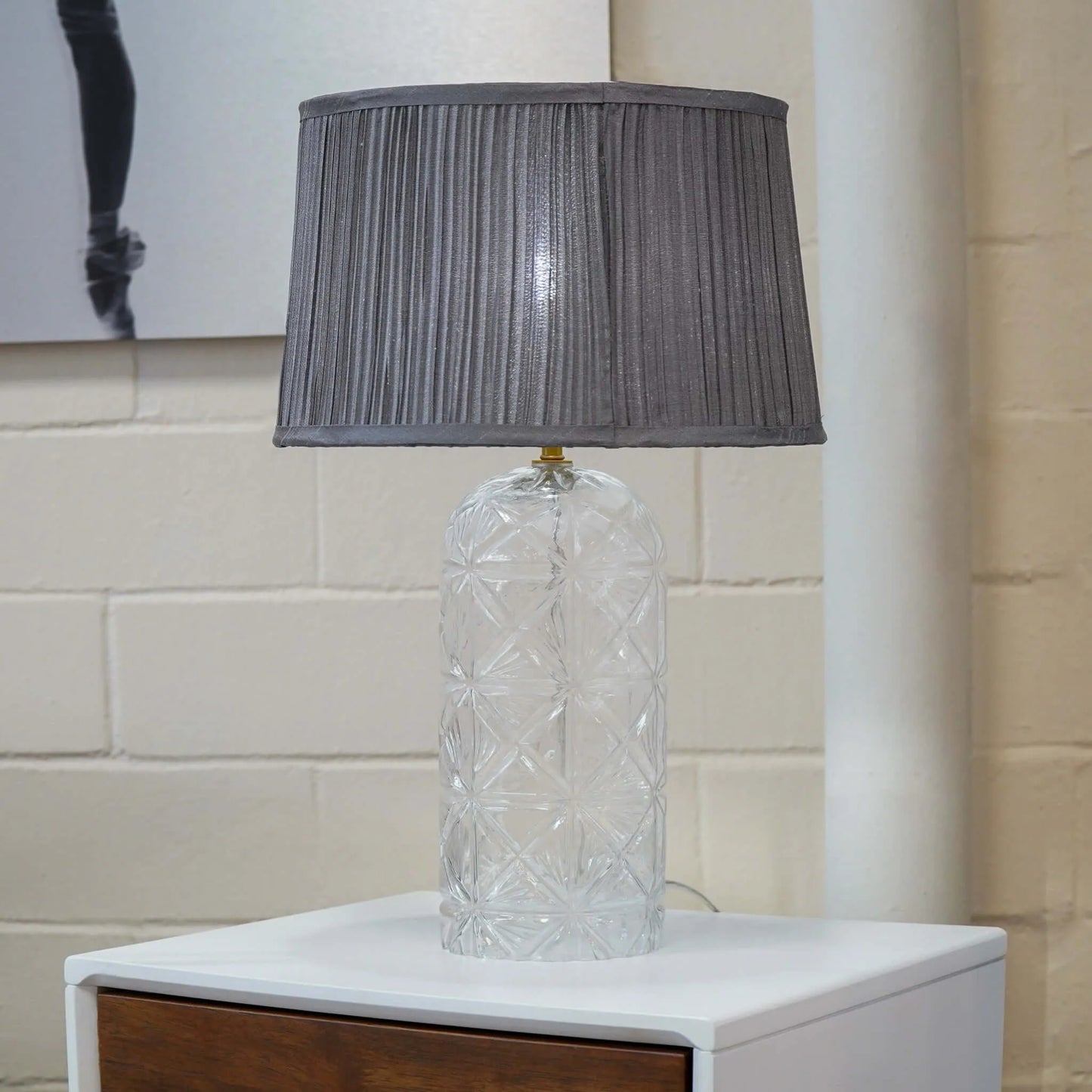 Table lamp with a textured gray shade on a white surface against a tiled wall.
