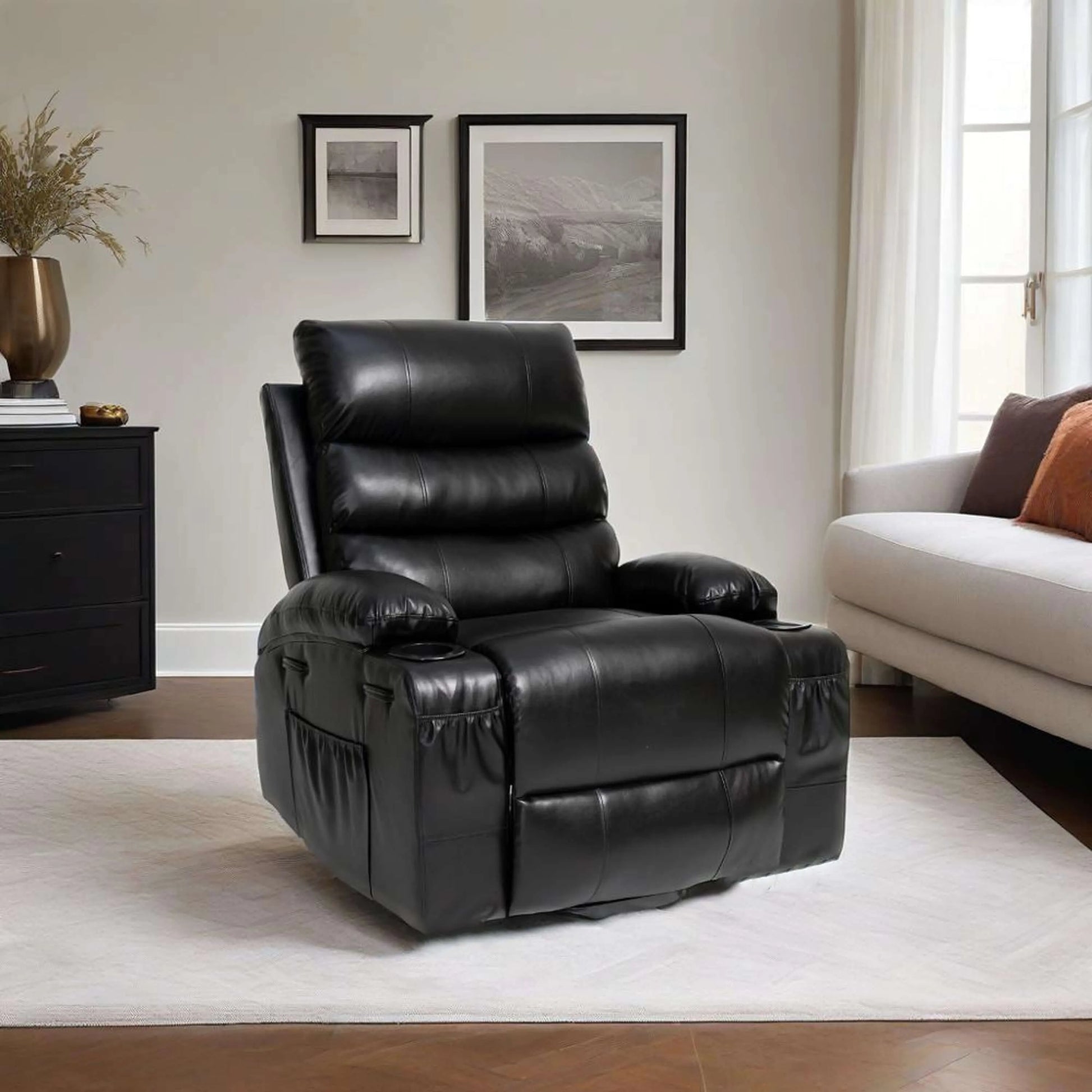 Black faux leather power lift recliner chair in a living room setting with a white sofa and framed pictures on the wall.