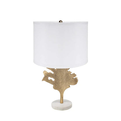 Table lamp with gold leaf design base and white shade on a white background