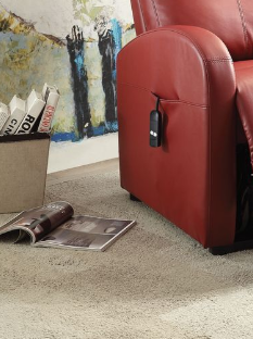 Close up of a red recliner chair in a living room setting with a magazine and remote control on the floor.