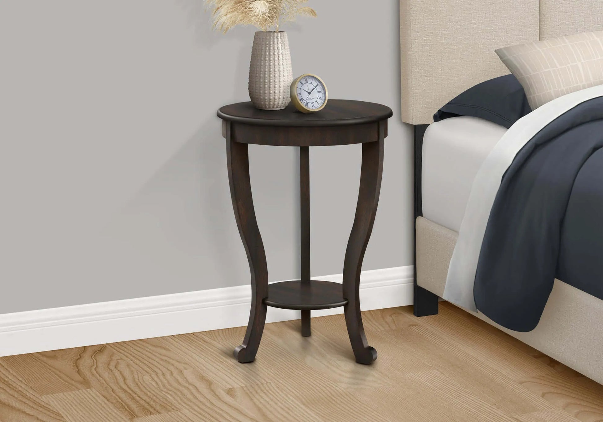 Small wooden side table with decorative items next to a bed in a bedroom setting.