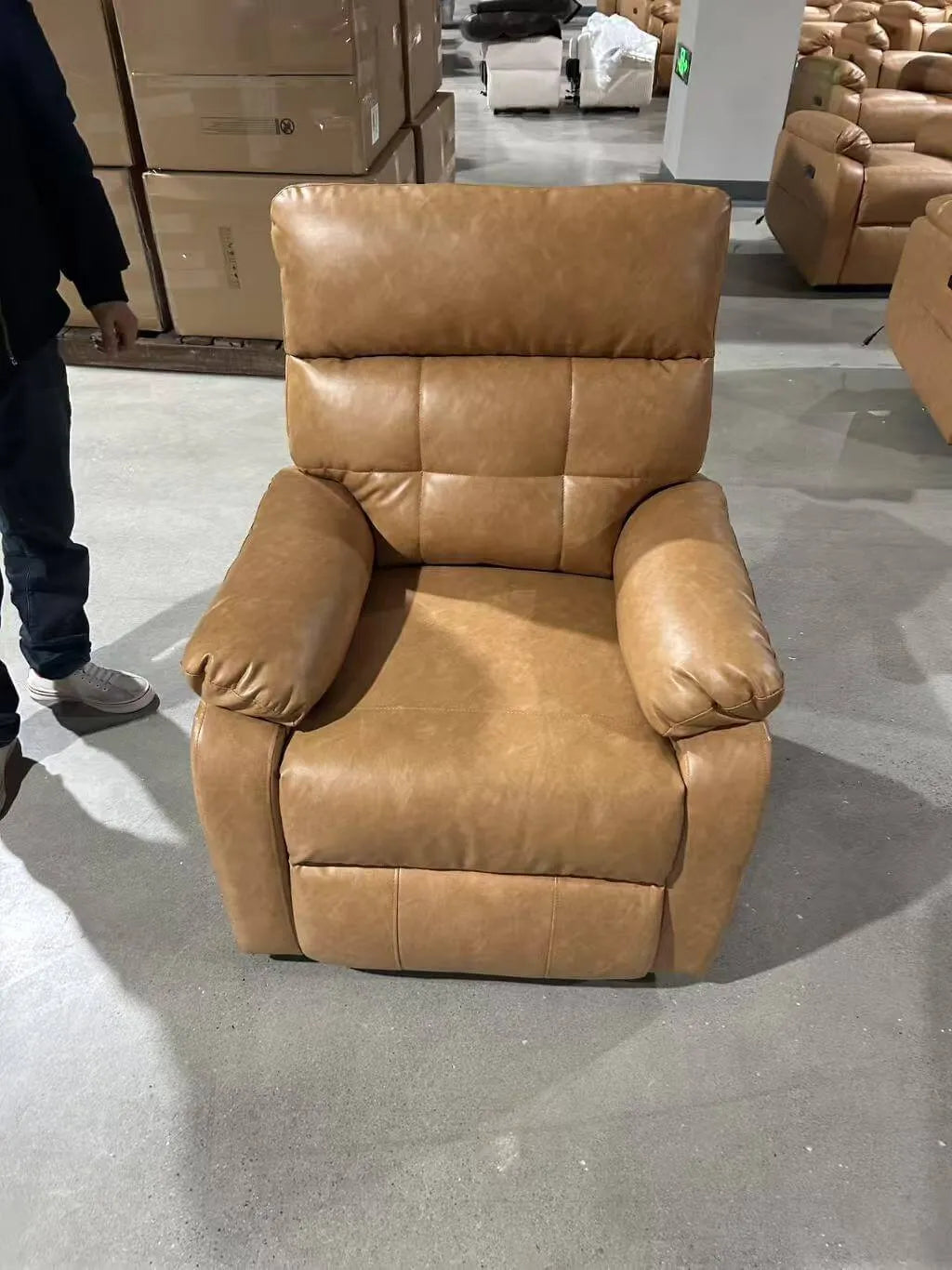 Brown leather recliner chair in a warehouse setting with boxes and another chair in the background.
