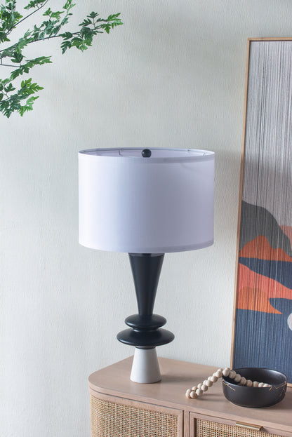 Table lamp with a white shade on a wooden side table against a light wall.