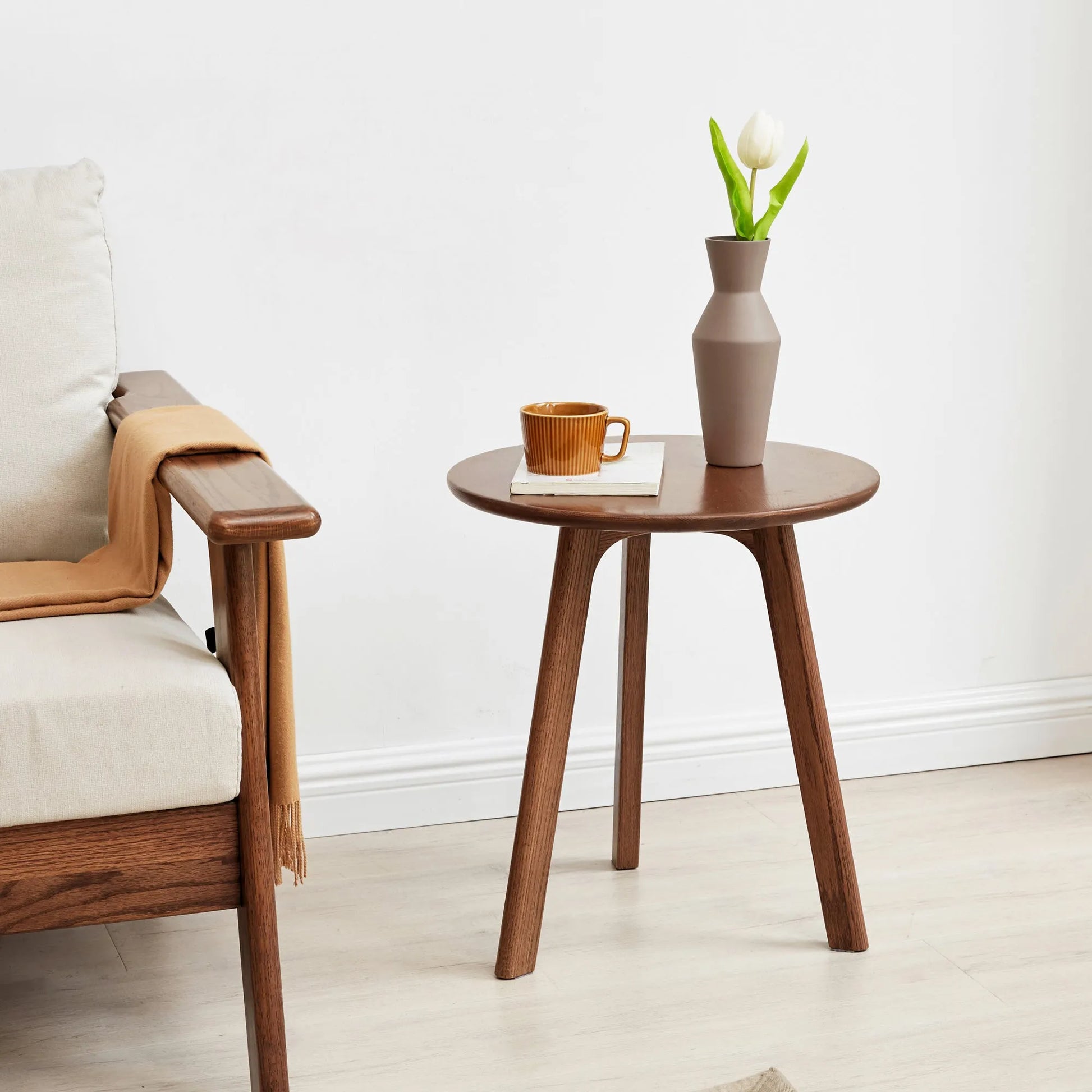 Wooden accent table with a vase and mug next to a chair in a minimalistic room.