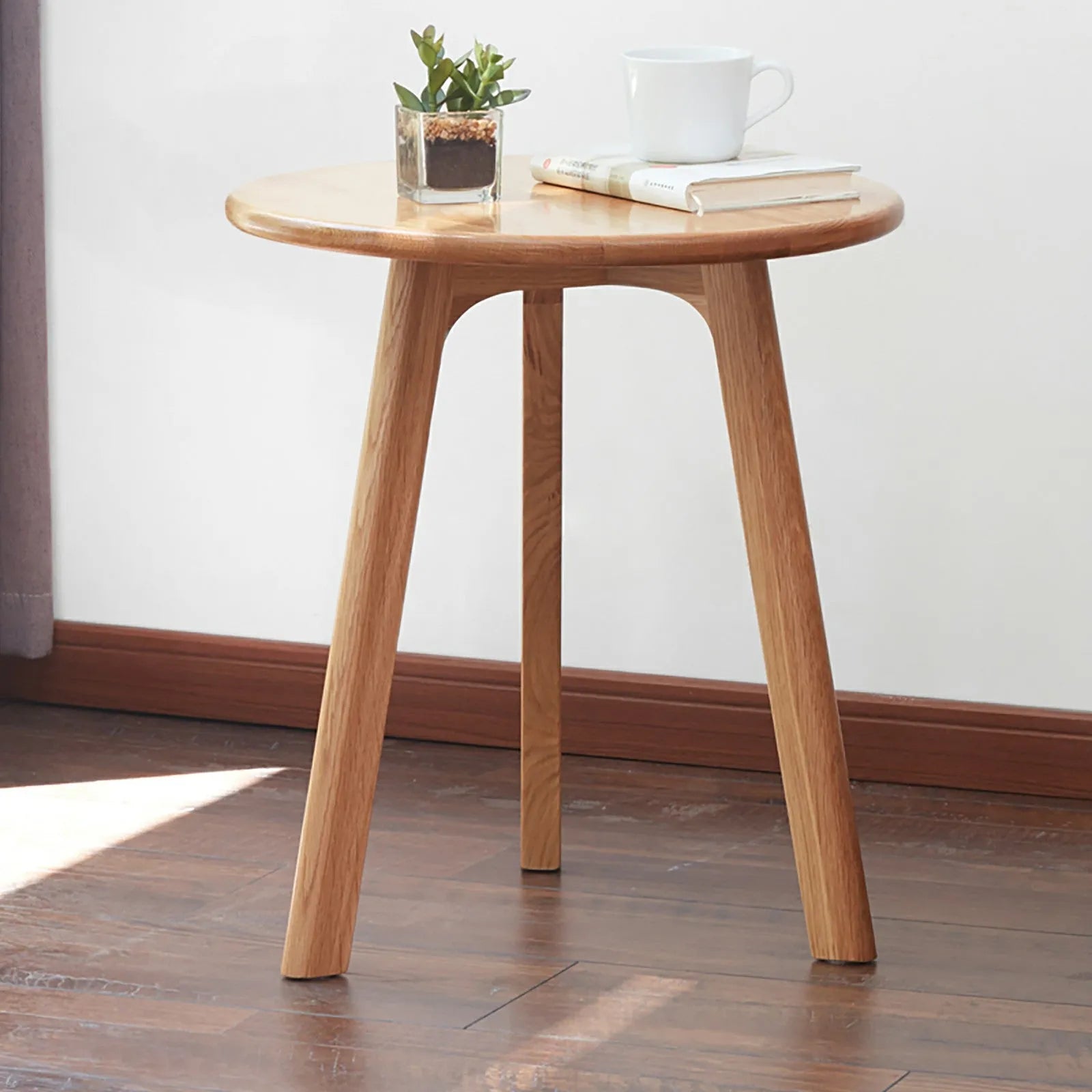 Wooden side table with a plant and books on a wooden floor.
