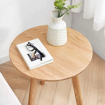 Round wooden end table with a book, glasses, and a vase on a light wood floor.