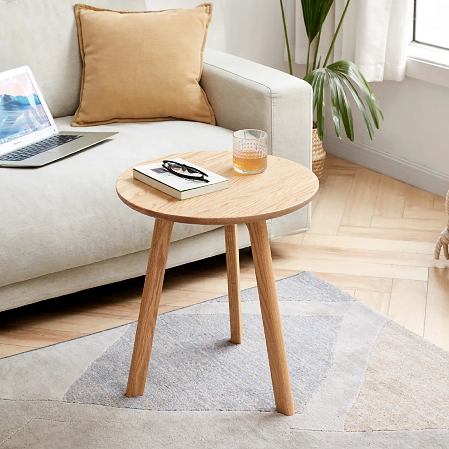 Wooden side table with a laptop, book, and glass in a living room setting.