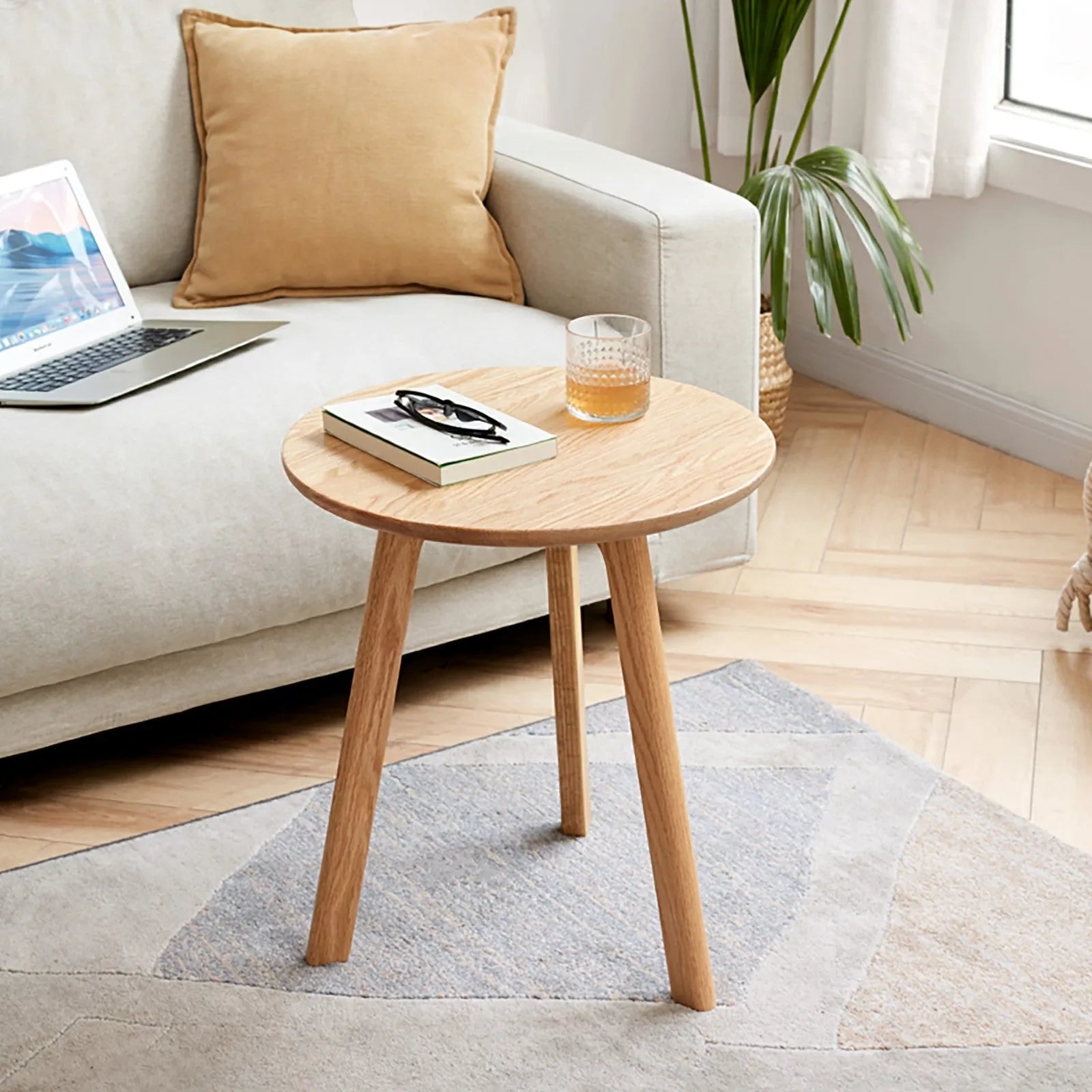 Wooden side table with a laptop, book, and glass in a living room setting.