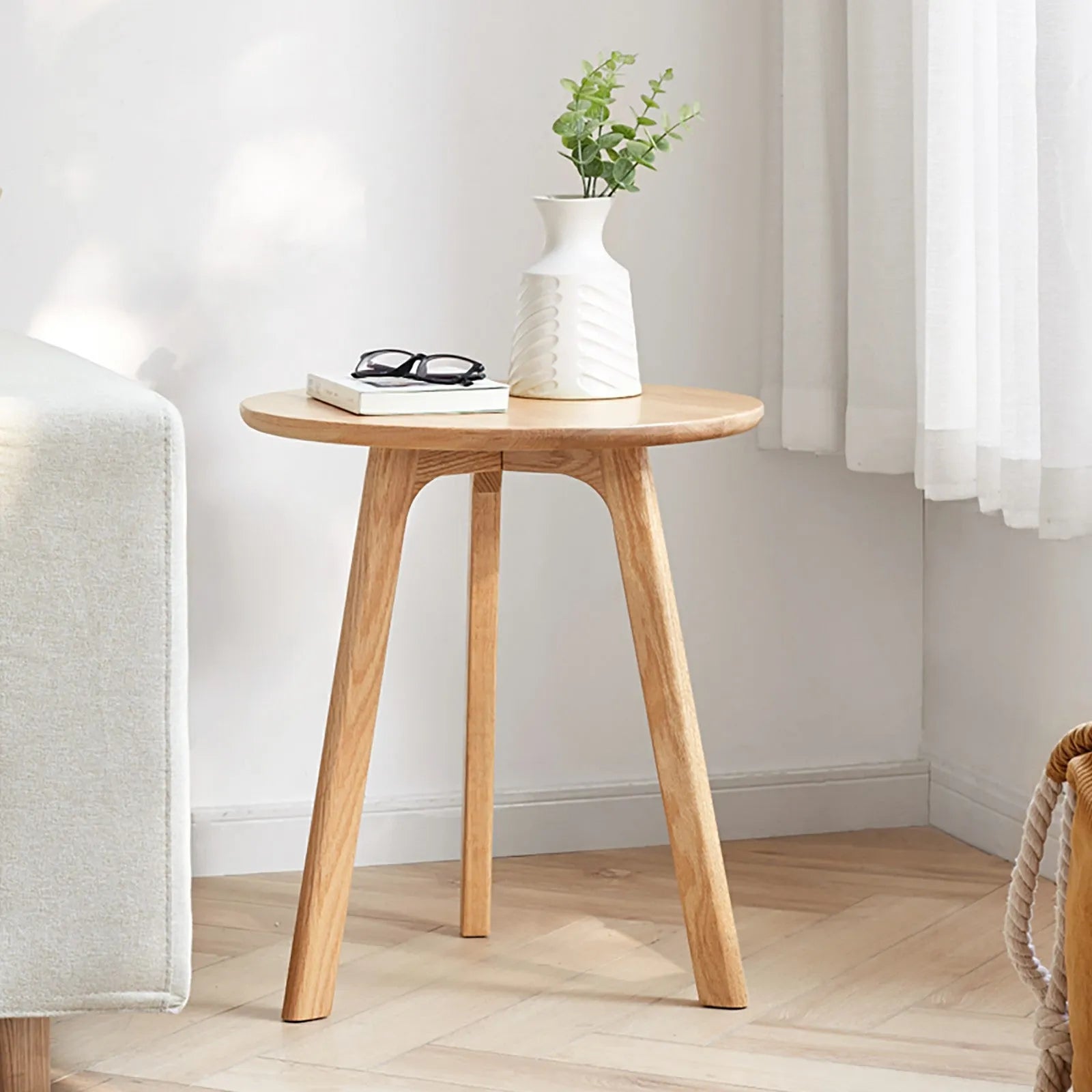 Wooden end table with a vase, books, and glasses in a room setting.
