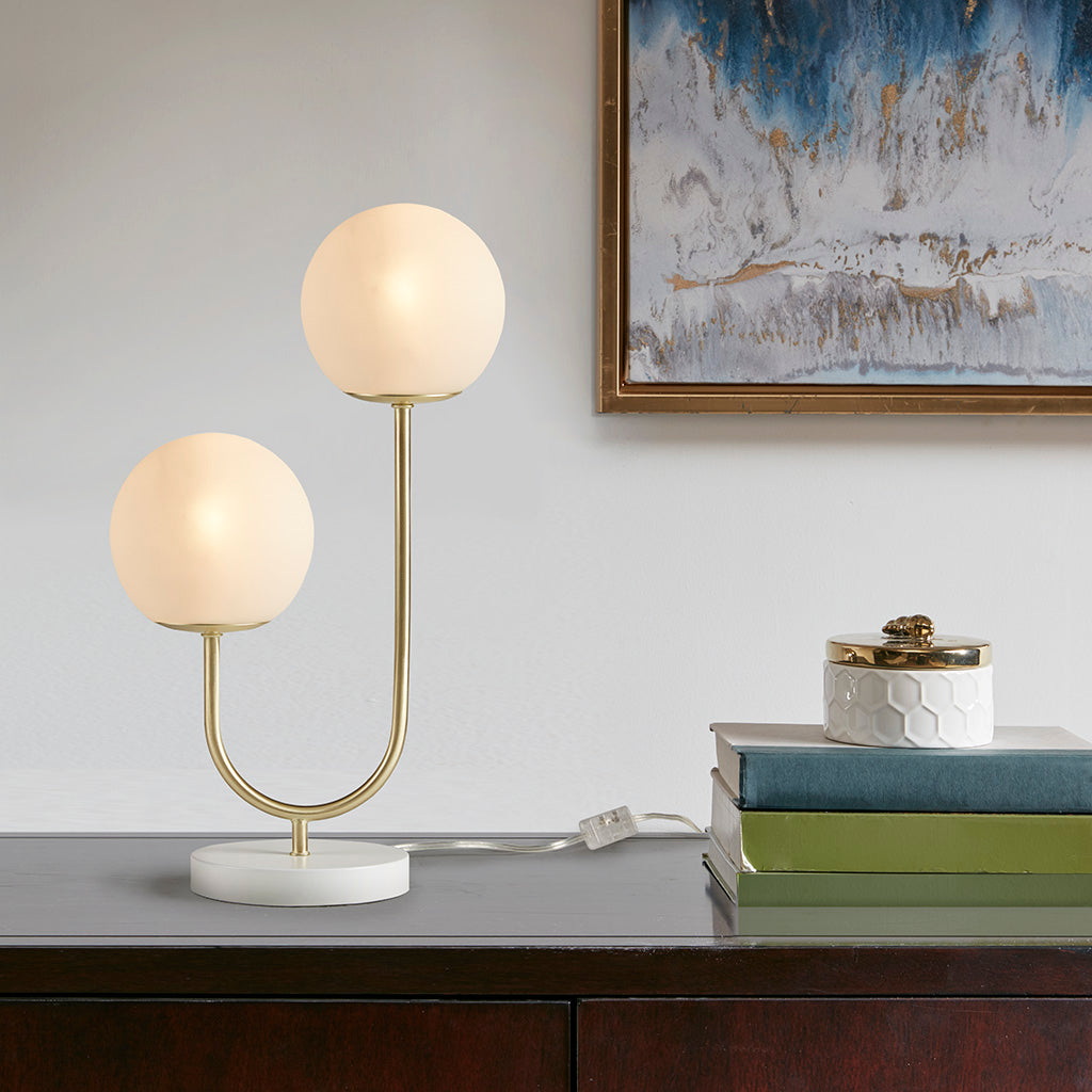 Modern table lamp with spherical glass shades on a desk next to books and a decorative box, with abstract art in the background.