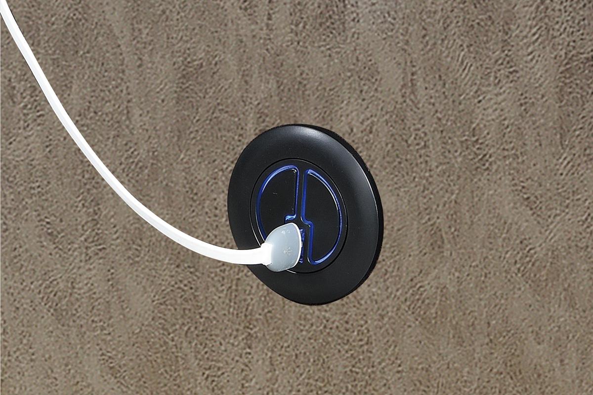 Black electrical outlet with white cord on a gray leather recliner chair.
