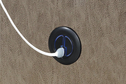 Black electrical outlet with white cord on a gray leather recliner chair.