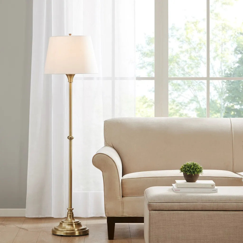 Living room with a beige sofa, floor lamp, and small table with a plant and books.
