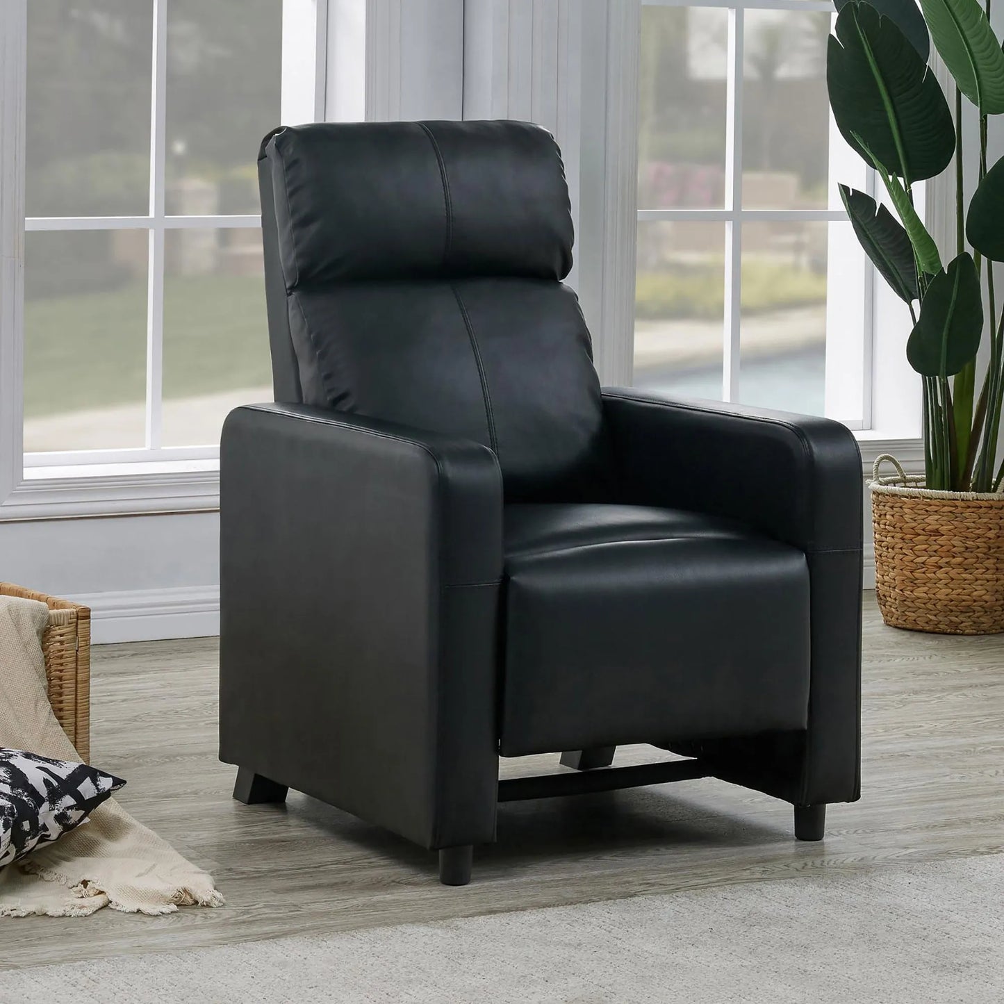 Black leather recliner chair in a living room setting with a plant and window in the background.