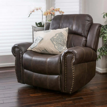 Brown faux leather glider recliner chair facing at a left angle with a decorative pillow in a room with plants and window blinds.