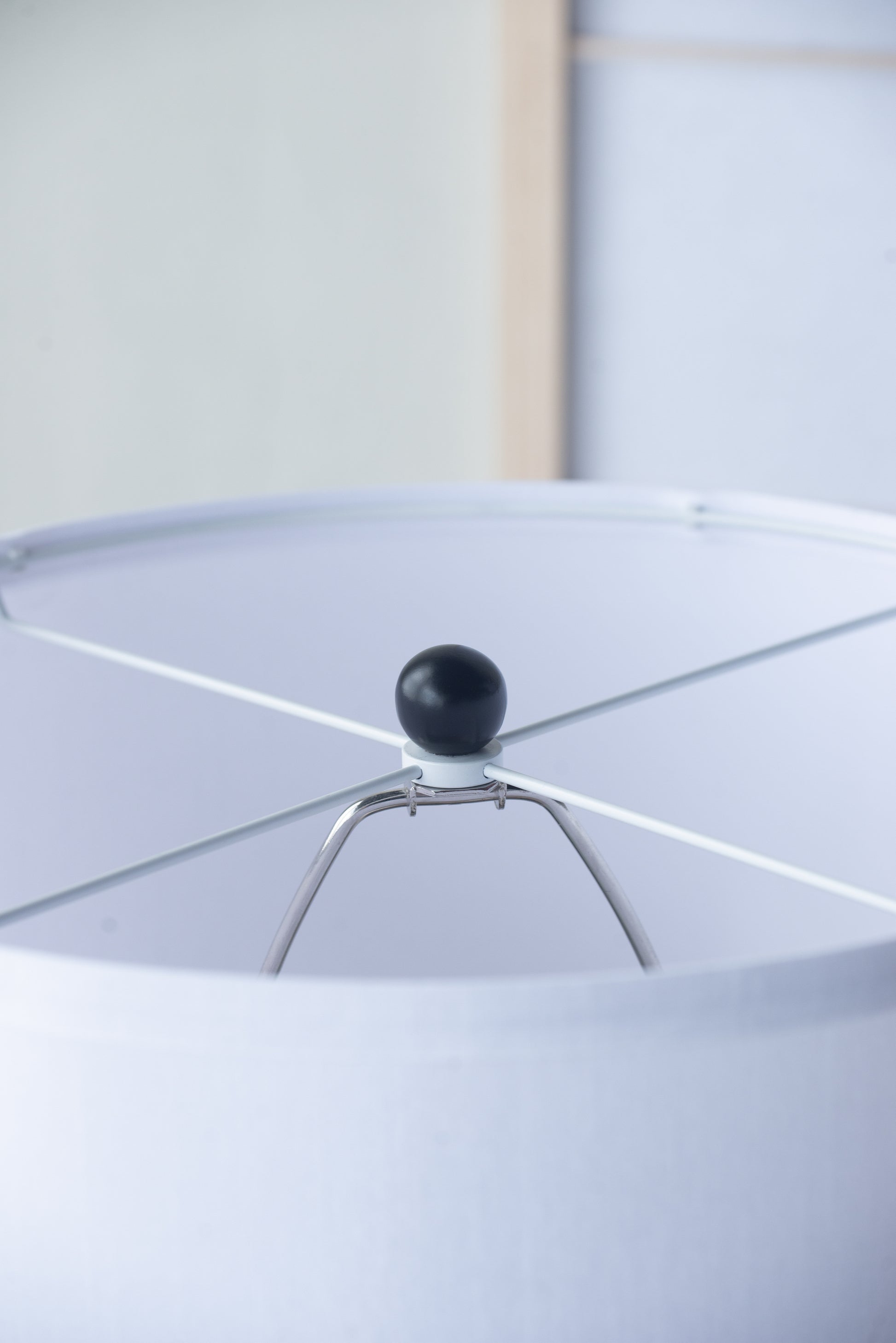 Close-up of a white lampshade with a black finial against a light background