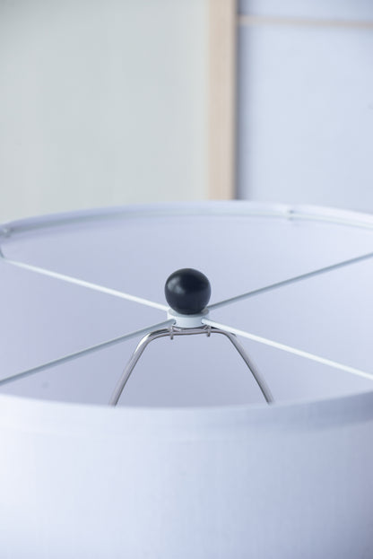 Close-up of a white lampshade with a black finial against a light background