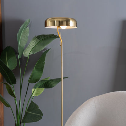 Gold floor lamp against a gray wall with a plant and chair in the foreground