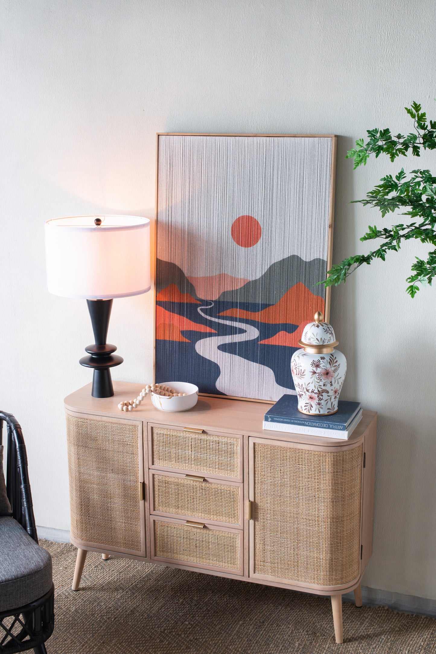 Lamp on a wicker sideboard with decorative items against a white wall