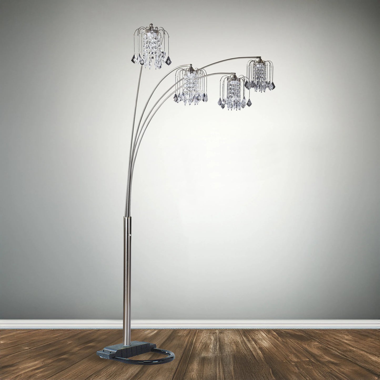 Arc floor lamp with crystal-like shades on a wooden floor against a gray wall.