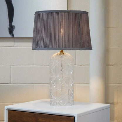 Table lamp with a textured gray shade on a white surface against a tiled wall.