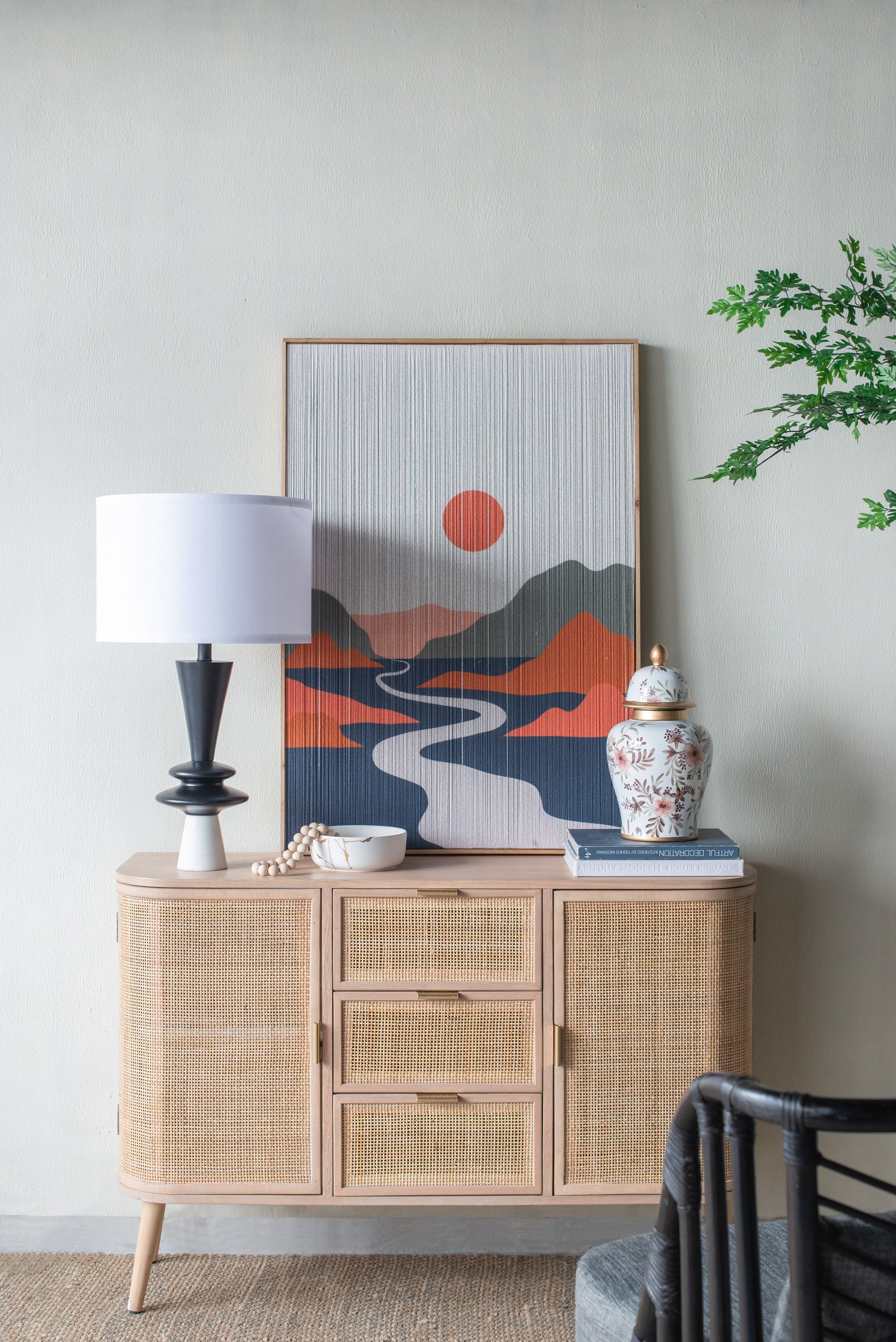 Table lamp on a wicker sideboard with decorative items including a vase and abstract art on a neutral wall.