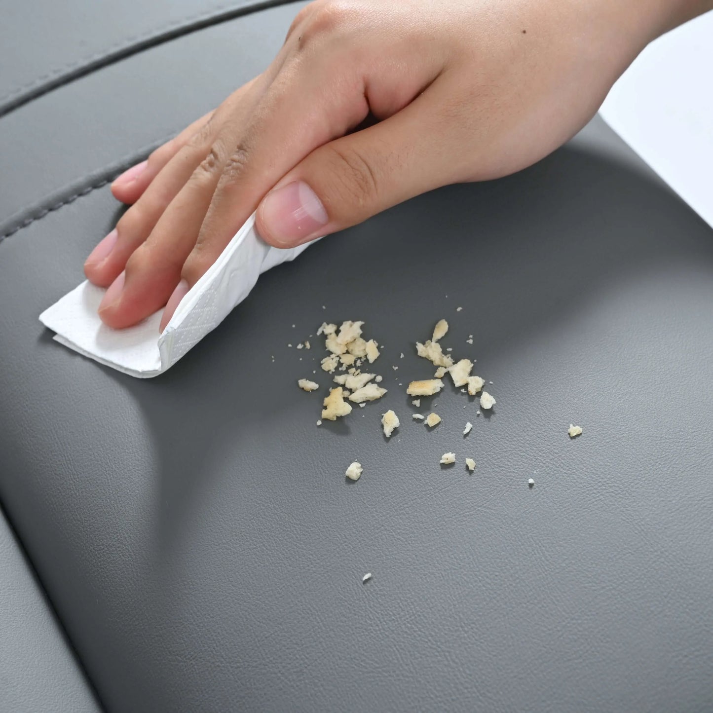 Hand using a cloth to wipe up small debris on a gray leather surface