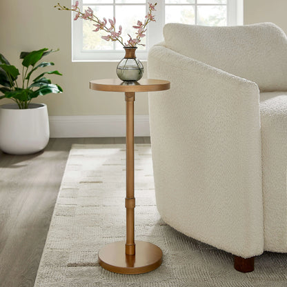 Antique brass end table with a vase of flowers next to a beige armchair in a living room.