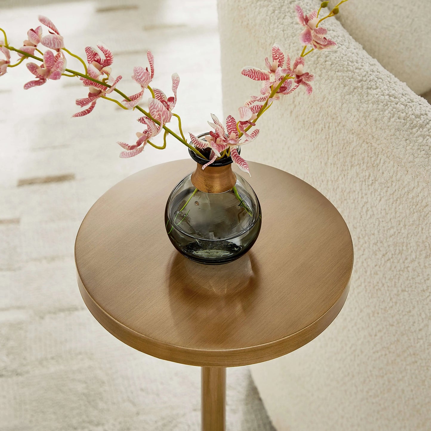Small round antique brass end table with a glass vase containing pink flowers on a light background