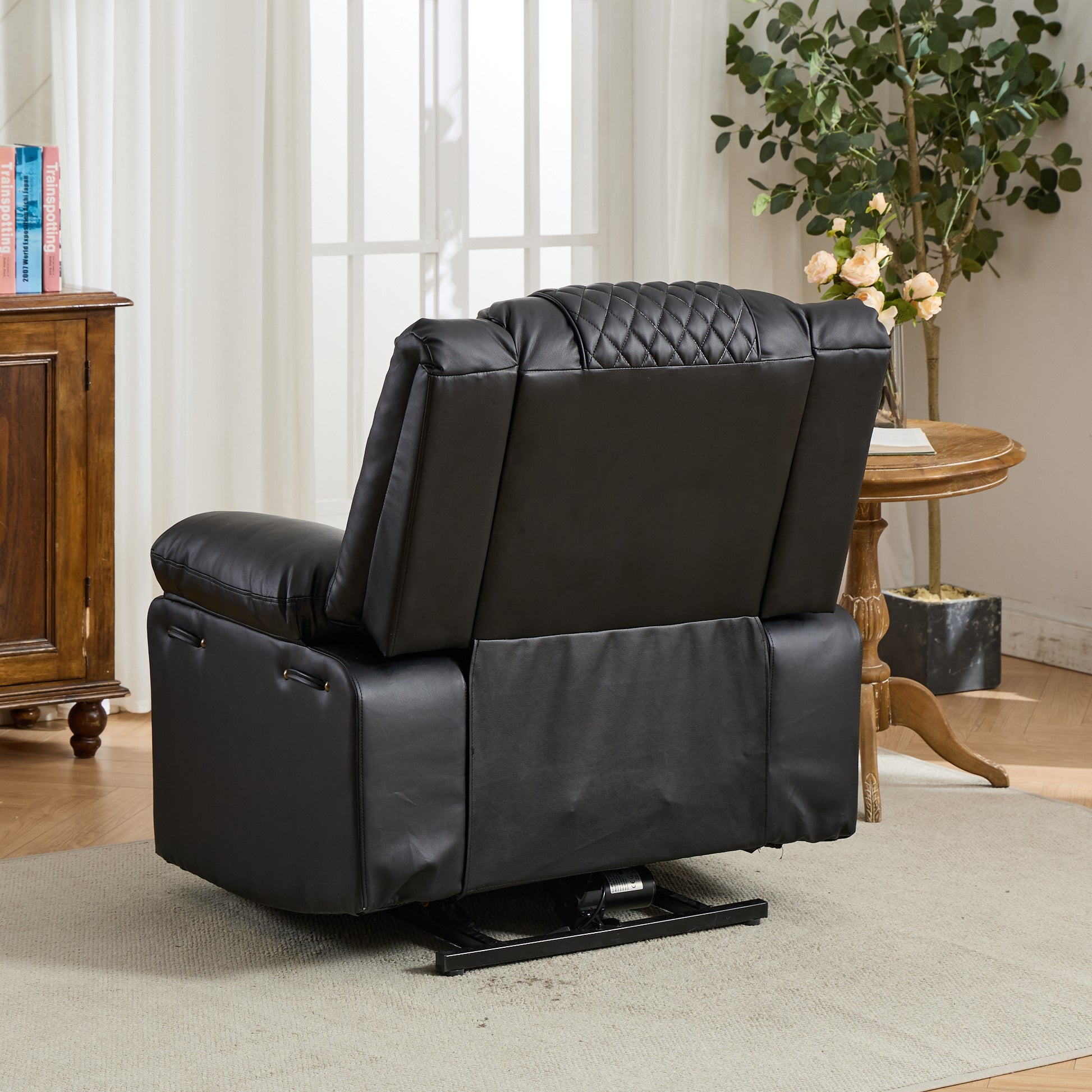 Black leather recliner chair in a living room setting with a wooden cabinet and potted plant.