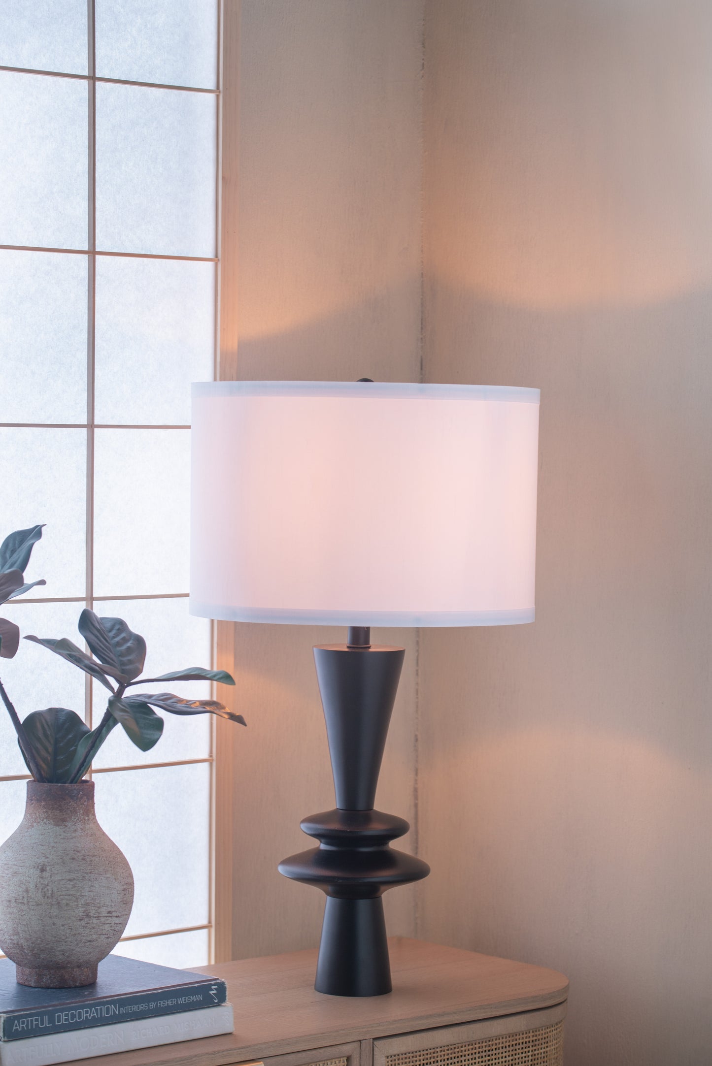 Table lamp with a white shade on a wooden surface next to a window