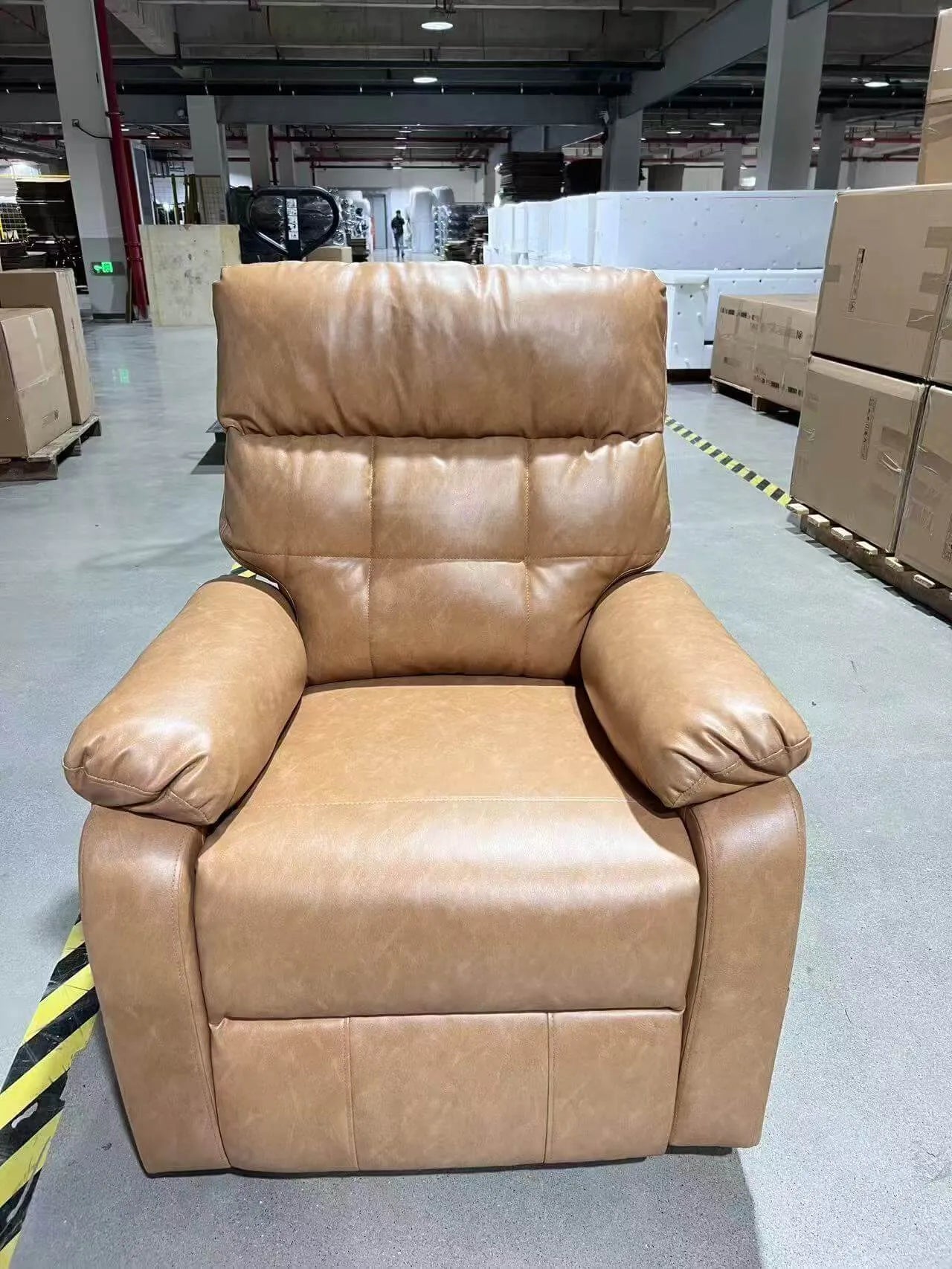Brown leather recliner chair in a warehouse setting with boxes and industrial equipment.