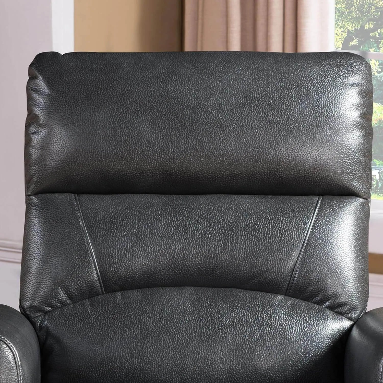 Black faux leather recliner chair in a room with beige curtains and a window.