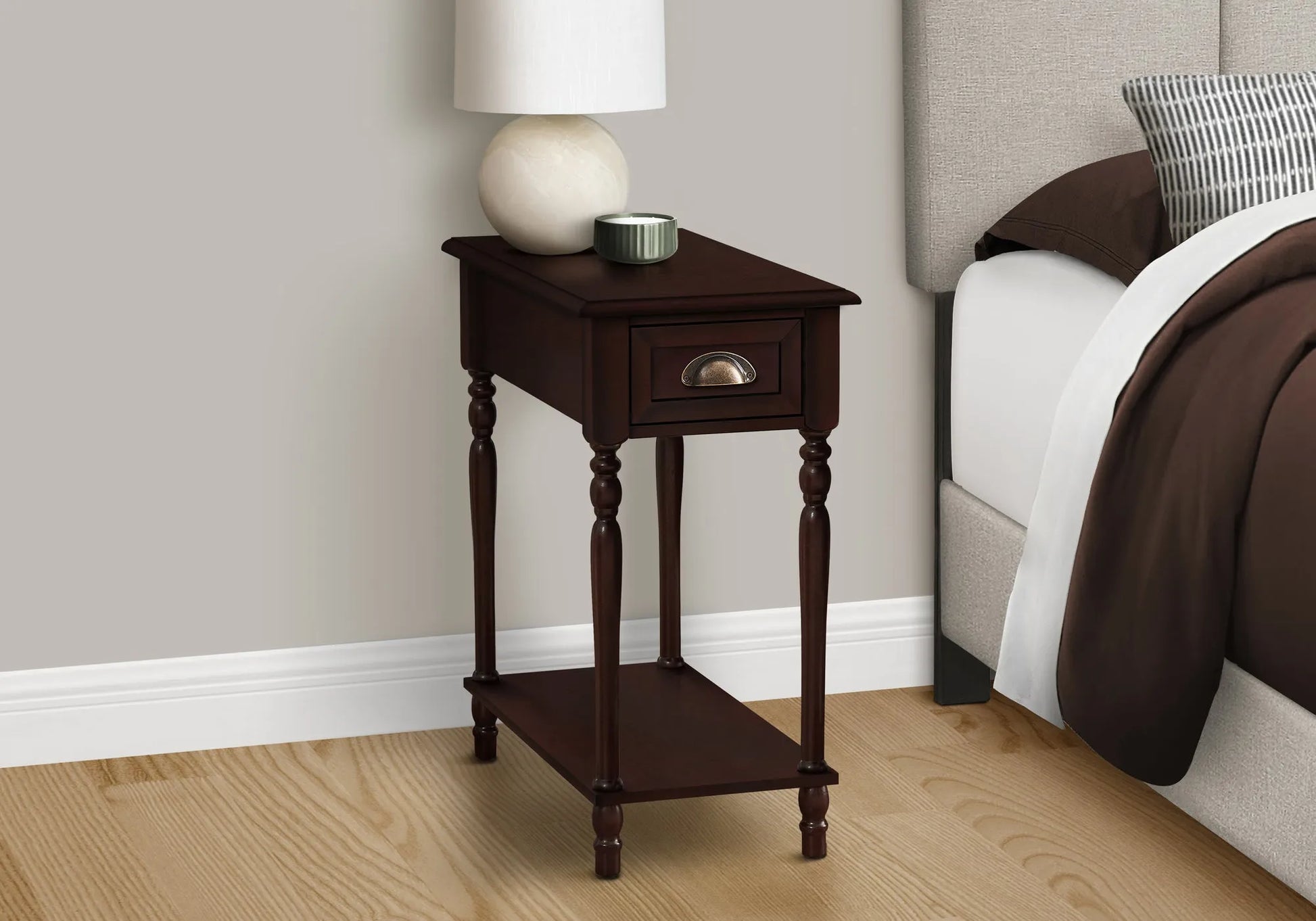 Wooden end table with a lamp and small container next to a bed with brown bedding.