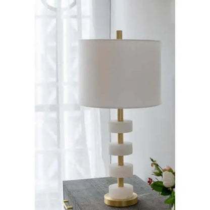 Table lamp with marble accents, gold base and white shade on a surface with a blurred background