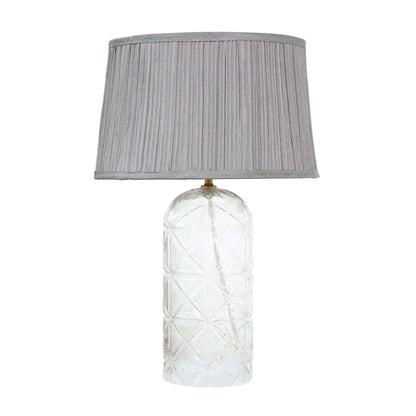 Table lamp with textured glass base and gray pleated shade on a white background