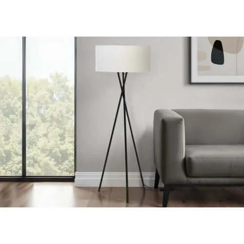 Tall floor lamp with metal legs and drum white shade in a living room setting.