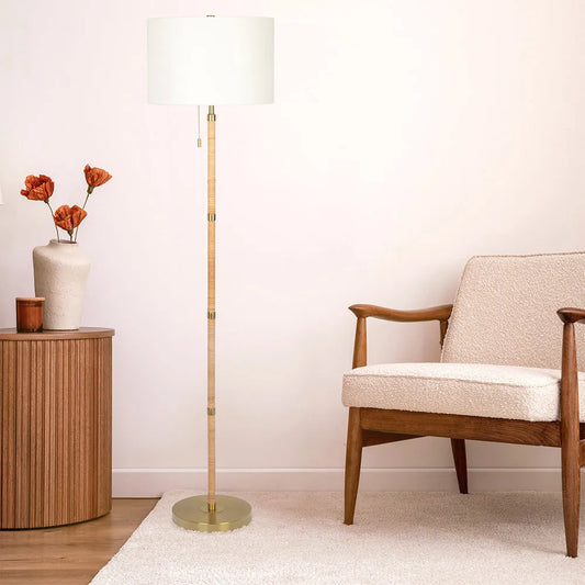 Floor lamp with a white shade next to a wooden armchair and side table with a vase of flowers.