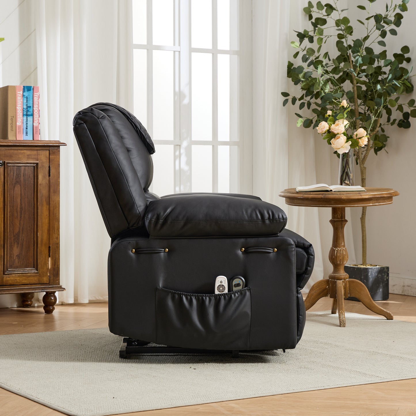 Black recliner chair with storage pocket and decorative detail in a living room setting with a wooden cabinet and table in the background.