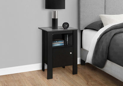 Black and grey end table with decorative items next to a bed with gray bedding.