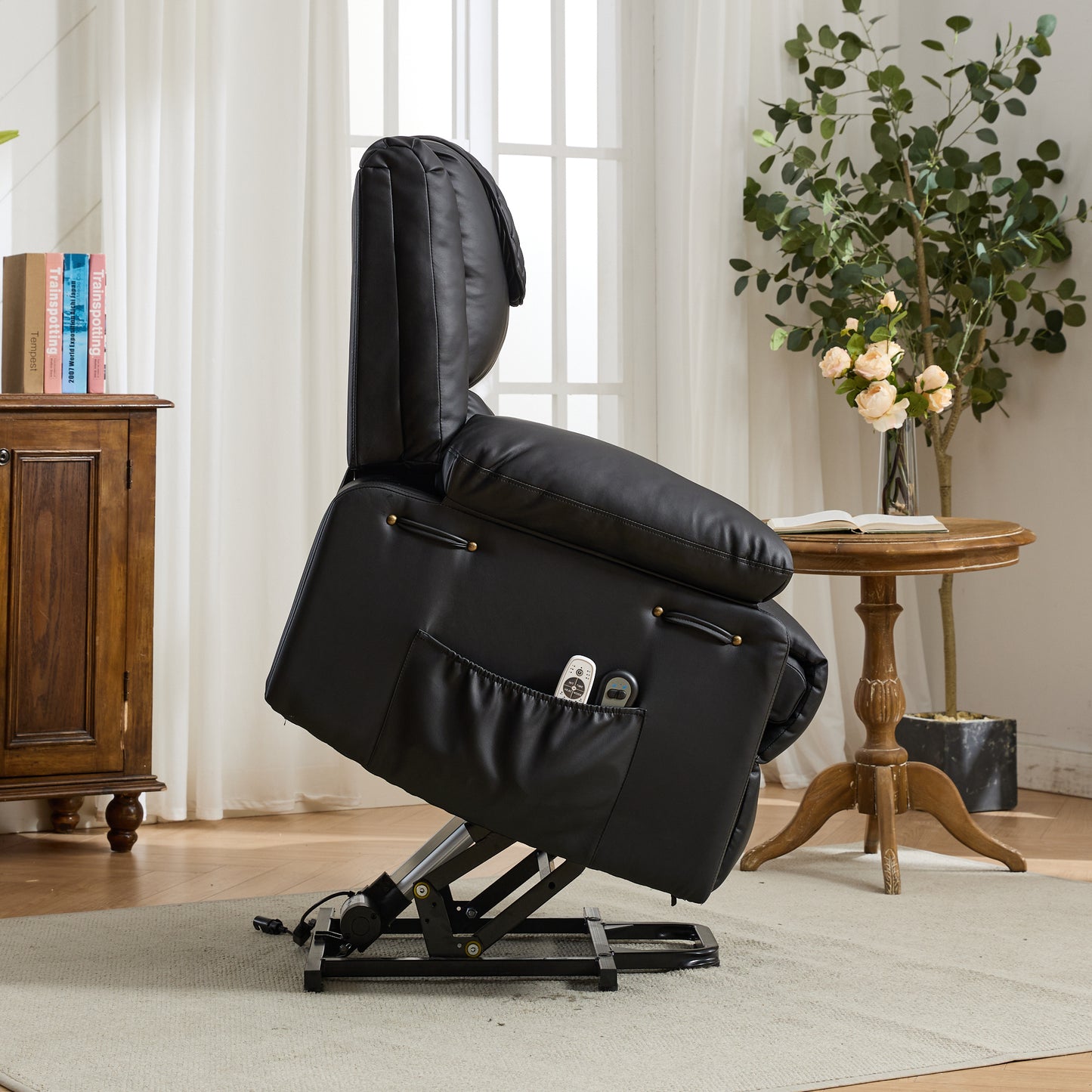 Black recliner lift chair fully extended in a living room setting with a wooden cabinet and plant.