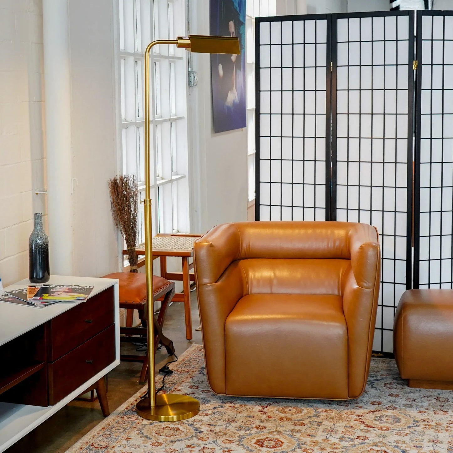 Brown leather armchair in a room with a gold floor lamp and decorative rug.