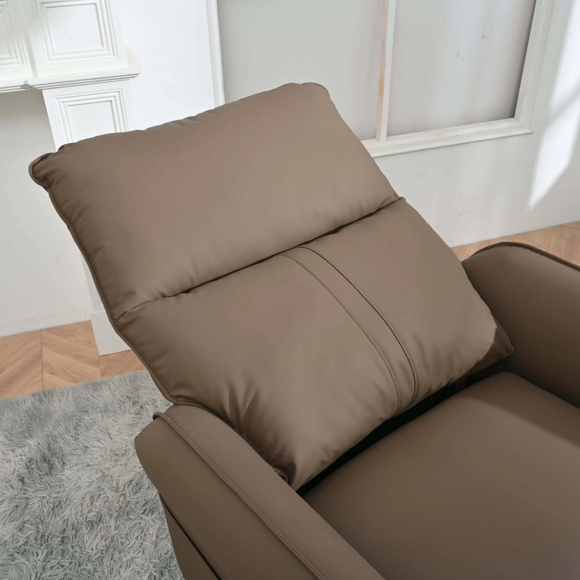 Close up of a brown recliner chair in a room with a light gray rug and white walls.