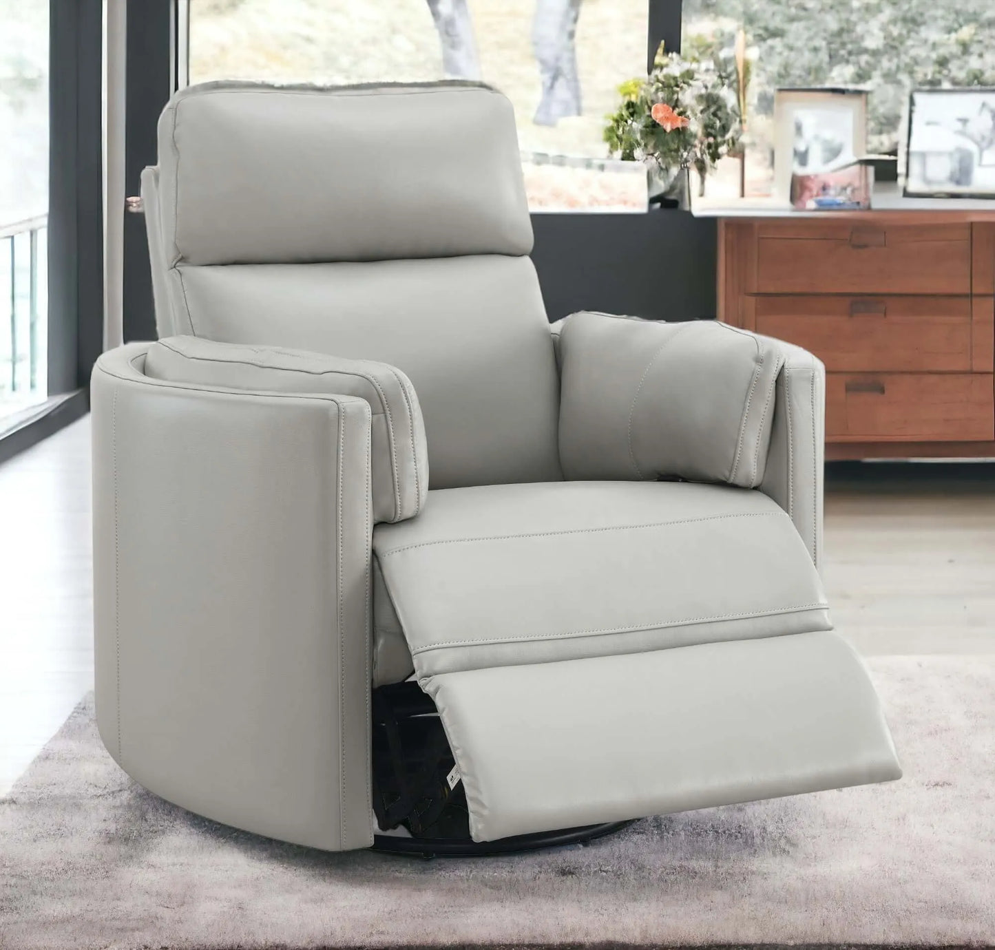 Close up of front angle view of the Sagen Gray Faux Leather Glider Recliner with Swivel with footrest slightly extended with a wooden cabinet behind and blury background.