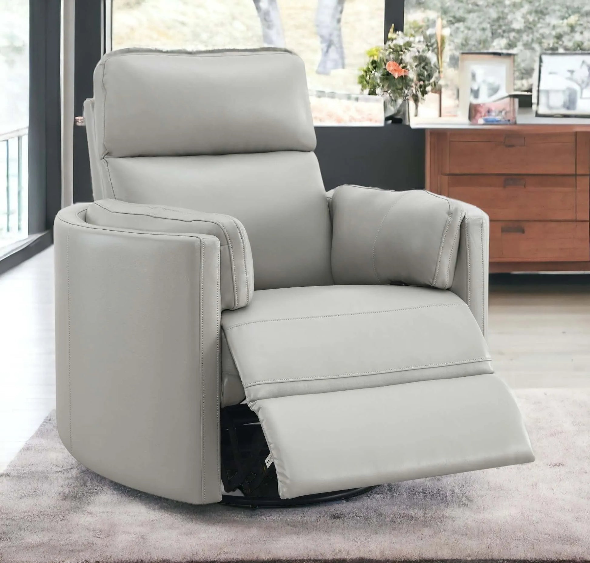 Close up of front angle view of the Sagen Gray Faux Leather Glider Recliner with Swivel with footrest slightly extended with a wooden cabinet behind and blury background.